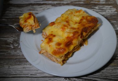 Baharatlı tavuk lazanyası basit beyaz bir tabakta duruyor. Katmanlarında erimiş altın peynir var. Çatallı, yumuşak ve lezzetli katmanlar ortaya çıkarır. Alacakaranlıkta herkesin damak zevkini tatmin etmeye hazır..