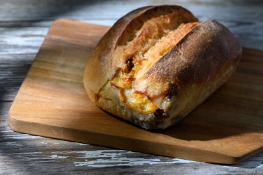 Sıcak, kabuklu bir ekmek somunu ahşap bir kesme tahtasına davetkar bir şekilde oturur, öğleden sonra güneşinin nazik parıltısıyla yıkanır, ev hissi uyandırır ve rahatlık verir..