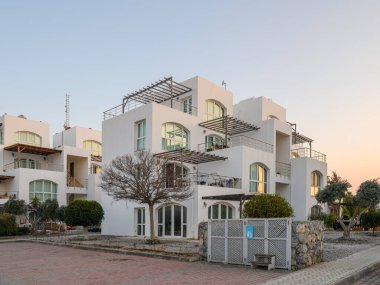 Geniş pencereli çağdaş binalar alacakaranlığın yumuşak parıltısında güneşleniyorlar, sakin bahçeler ve patikalarla çevrili..