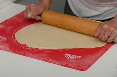 Eller ustalıkla hamuru parlak, işaretli bir yüzeye serer. Mutfak atmosferiyle çevrili. Taze pişmiş ürünlerin vaadiyle dolu..