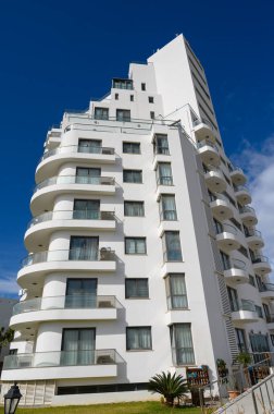 Güneşli bir şehir ortamında yükselen bu çarpıcı bina, çağdaş bir yaşam tarzı ve canlı şehir ruhunu yansıtan kıvrımlı balkonlar içeren zarif ve modern tasarımıyla büyüleyicidir..