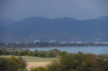 Sakin kıyı manzarasının ortasında, yaklaşan fırtınayı işaret eden kara bulutlar dağların üzerinde toplanıyor. Huzurlu dalgalar kıyıları öpüyor, gökyüzündeki gerilime zıt..