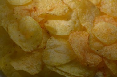 Altın patates cipsleri üst üste yığılmıştı. Çıtır çıtır yüzeyleri ışığı çok güzel yakalıyordu. Davetkar dokular, her türlü atıştırmalık için mükemmel, tatmin edici bir çıtırtı olduğunu gösteriyor..