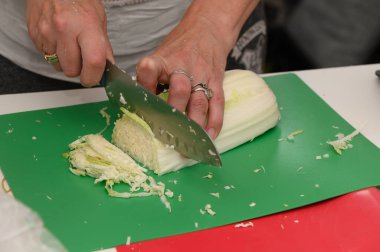 Canlı yeşil bir kesme tahtasının üzerinde marifetli bir şekilde lahana doğrayan eller, canlı bir mutfak ortamında lezzetli bir yemek oluşturur..