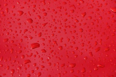 Parlak kırmızı bir yüzey üzerinde parlayan yağmur damlaları güzel bir kontrastı ve neşeli, taze bir atmosfer yaratır..