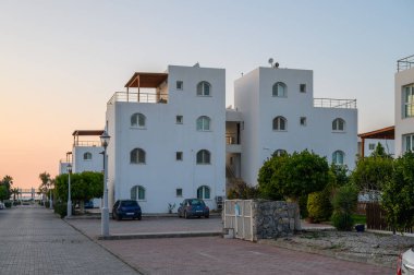 Beyazlatılmış yapılar, arka planda güneş batarken liman boyunca huzurlu bir atmosfer yaratıyor..