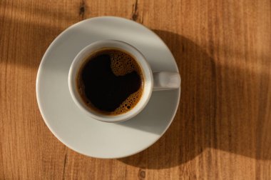 Dumanı tüten bir kahve fincanı, ahşap bir yüzeyde narin bir şekilde duruyor, sabah ışığının yumuşak parıltısında güneşleniyor..