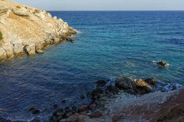 Sakin deniz kıyısında dinlenin. Dalgalar yavaşça kayalık kıyılara doğru sarkan günbatımının altında süzülürken..