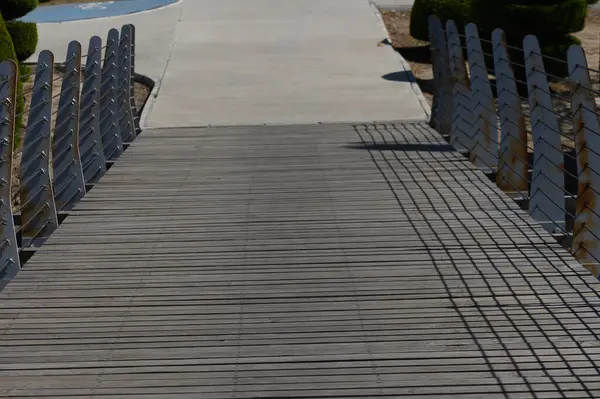 Huzurlu bir parkta huzurlu bir yol üzerinde güzel yapılmış ahşap bir köprü uzanır. Gölgeler, güneşli bir günde sakin yürüyüşler yaparak sahil boyunca zarifçe uzanır..