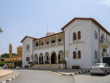 Ziyaretçiler, kemerli camları ve yakınındaki taş çan kulesi olan beyaz bir binanın zarif tasarımına hayran. Açık mavi gökyüzü davetkar atmosfere ekleniyor. Keşif için mükemmel..