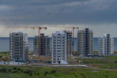 Çağdaş gökdelenlerin inşaatı okyanus kıyısında bulutlarla dolu dramatik bir gökyüzünün altında gerçekleşir..