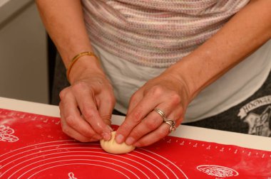 Sadık bir fırıncı küçük bir hamur topunu ustalıkla şekillendirir, rahat bir mutfak atmosferinde zanaatkarlık sergiler..