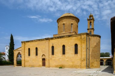 Açık mavi gökyüzünün ortasında, tarihi bir taş kilise gururla duruyor, karmaşık tasarım detaylarını gözler önüne seriyor. Sıcak güneş ışığı, ziyaretçilerin çarpıcı çevreye hayran kaldığı yaşlanmış dış görünüşünü ön plana çıkarıyor..