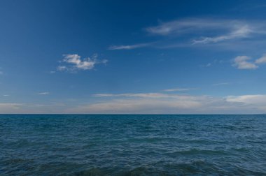 Yumuşak dalgalar derin mavi sularda dalgalanır, sonsuz gökyüzü ile kusursuz bir şekilde harmanlanır. Yumuşak bulutlar tembelce tepemize doğru sürükleniyor. Bu da sakin sahilde huzurlu bir gün geçirdiğimizi gösteriyor..