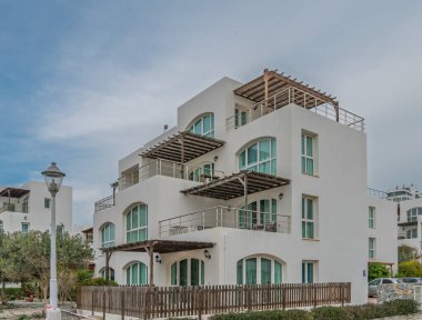 Şık kıyı binası, çok sayıda teras ve geniş pencerelere sahip, dingin bir gökyüzünün arka planına karşı kurulmuş..