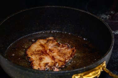 Sulu bir domuz pirzolası, dökme demir bir tavada kızarıyor. Sıcak mutfağı dolduran lezzetli kokular yayıyor..
