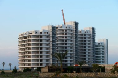 İnşaat işçileri, güneş ufukta batarken parlak bir kıyı yüksekliğini bitirmekle meşguller..