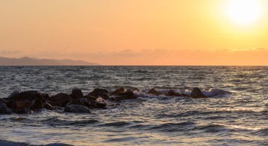 Kıbrıs 'ta sakin bir plajın üzerinde canlı turuncu ve pembe bir gün batımı, yumuşak dalgalar ve sıcak akşam ışığı. Deniz kenarında huzurlu mükemmel bir an..