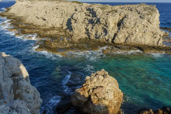 Engebeli uçurumlar, batan güneşin sıcacık parıltısıyla boyanmış berrak turkuaz sulardan keskin bir şekilde yükselir..