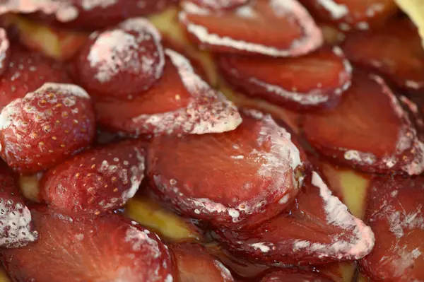 Dilimlenmiş çileklerden oluşan canlı bir düzenleme bozulmuş bir pastada şerbetle parlıyor, lezzet tomurcuklarını yaz mutluluğunun tatlı tatlarını tatmaya davet ediyor..