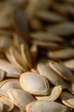 Yakından bakınca taze toplanmış balkabağı tohumlarının narin dokusunu ve ılık tonlarını doğal ışık altında gösterir..