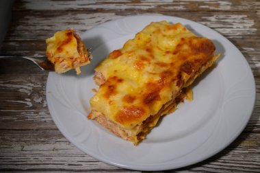 Beyaz bir tabağa konmuş nefis ev yapımı lazanya makarna, et ve erimiş peynir katmanları sergileniyor. Bir çatal bir porsiyon tutar, bu doyurucu yemeğin tadına ve tatmine davet eder..