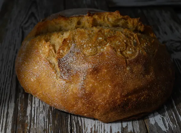 Altın kabuklu somun ekmek yıpranmış ahşap üzerine oturur, sıcaklığı ve taze pişmiş nefis kokusuyla davet eder..