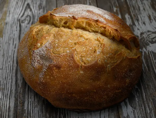 Altın-kahverengi kabuklu ekmek, taze pişmiş nefis bir koku yayarak, eski ahşap yüzeyde yatar..
