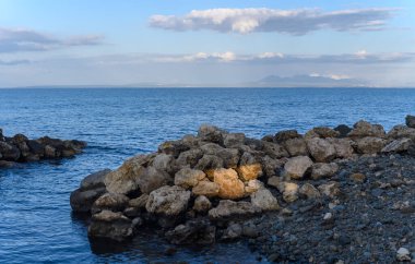 Sakin sulardan engebeli kayalar çıkar. Yumuşak bulutlar, alacakaranlık anlarında geniş bir gökyüzünde sürüklenir..
