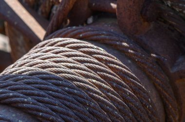 Çarpık çelik kablolar parlak güneşin altında parlayarak pas ve yıpranma izlerini ortaya çıkarır. Ağır makineler eski bir sanayi bölgesinde zamanın ve emeğin bir göstergesi olarak duruyor..