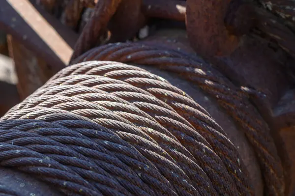 Çarpık çelik kablolar parlak güneşin altında parlayarak pas ve yıpranma izlerini ortaya çıkarır. Ağır makineler eski bir sanayi bölgesinde zamanın ve emeğin bir göstergesi olarak duruyor..