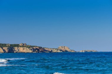 Güneş sakin denizin üzerinde batmaya başlarken dalgalar yavaşça kayalık kıyı şeridine çarpar ve gökyüzünü boyarlar..