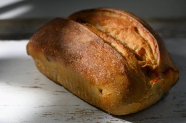 Güzel bir somun hünerli ekmek, yumuşak doğal ışığın sıcaklığının tadını çıkaran, kırsal ahşap bir masada oturur. Yakınındaki herkesi lezzetli aromasının ve çıtır çıtır kabuğunun tadını çıkarmaya davet eder..