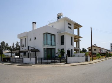 Barışçıl bir caddenin köşesinde büyük cam pencereler ve minimalist tasarımlarla dolu çağdaş bir ev gururla duruyor. Güneş ışığı yapıyı yıkıyor, zarafetini arttırıyor..