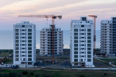 Renkli bir gökyüzüne karşı vinçlerle kaplı modern apartman binalarının inşaatı devam ediyor.