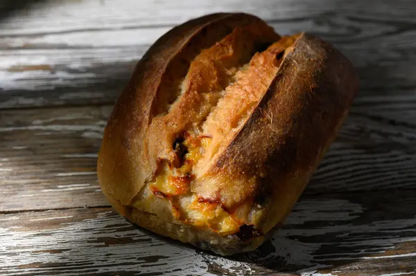 Altından kabuklu güzel fırınlanmış bir somun, kırsal cazibesini yıpranmış ahşap bir masada sergiliyor. Ekmeğin sıcak tonları davetkar bir atmosfer yaratıyor, samimi bir toplantı için mükemmel..