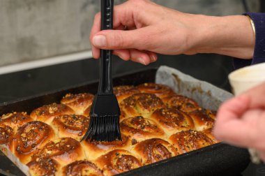 Sıcak rulo fırından çıkar eller dikkatlice fırçalarken tereyağını altın-kahverengi tepelerin üzerine eritir. Bir fındık serpintisi, aile bir araya gelip birlikte pişmiş hazzın tadını çıkarırken aromayı güçlendirir..