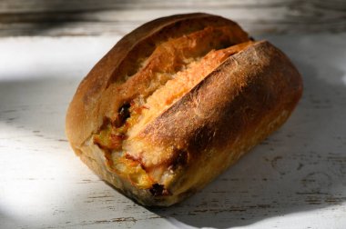 Sıcak, altın zanaatkar ekmek, yumuşak güneş ışığıyla yıkanmış, ahşap bir masada oturur. Kabuğun dokusu taze, ev yapımı doğasını ön plana çıkarıyor, herkesi lezzetinin tadını çıkarmaya davet ediyor..