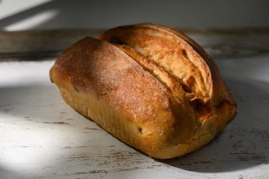 Kıtır kıtır ekmek, eskimiş bir masaya davetkar bir şekilde oturur. Sıcak öğleden sonra güneşi dokusunu ve sıcaklığını arttırırken yumuşak gölgeler etrafında dans ediyor..