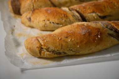 Parşömen kağıdının üzerine uzanmış altın sarısı zanaatkar somunları kırsal dokularını ve lezzetli aromalarını gözler önüne seriyor. Mutfağın sıcak atmosferi taze fırının davetkar manzarasını güçlendirir..