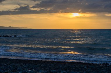 Kıbrıs kıyıları boyunca uzanan uzak dağları olan sakin bir Akdeniz üzerinde gün batımı ışığı. Huzurlu kıyı manzarası rahatlama ve seyahat kavramları için mükemmeldir.