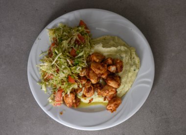 Yumuşak patates püresi ve taze lahana ve olgun domates salatasıyla birlikte servis edilen baharatlı tavuk parçalarının tadını çıkarın. Rahatlatıcı yemek severler için mükemmel..