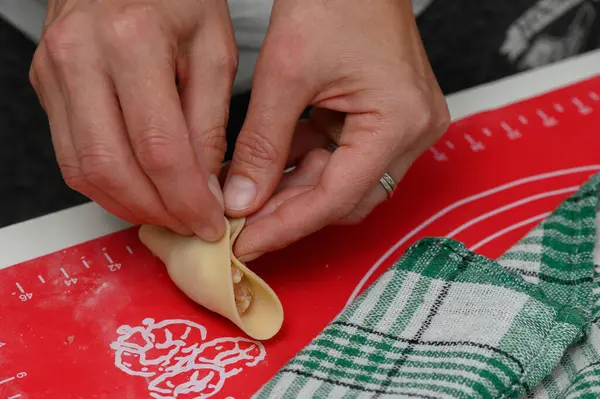 Eller hamuru, yeşil kareli kumaş ve bir tutam unla çevrili canlı kırmızı bir tezgahın üzerine ustalıkla katlar. Mutfak yaratıcılığının neşesini yakalar..