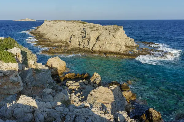 Güneş batarken engebeli kayalara doğru yumuşak dalgalar süzülüyor. Sakin kıyı sularına sıcak renkler döküyor..