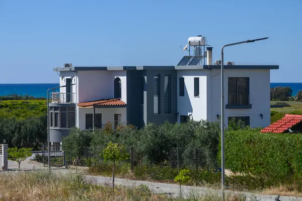 Modern bir villa, mavi bir okyanusun zeminine ve bereketli manzaralara karşı, güneş ışığını yansıtan görkemli bir şekilde durmaktadır. Şık tasarımı ve yakınındaki yeşillik huzurlu bir ortam yaratıyor..