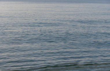 Hafif dalgalar kıyıya vurur, akşam gökyüzü suyun kenarına yaklaşırken huzurlu bir atmosfer yaratır..