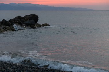 Güneş ufkun altına batar, durgun denizde pembe ve turuncu renkler bırakır. Yumuşak dalgalar kayalık kıyı şeridini okşayarak bu sahil çekilmesinde barışçıl bir atmosfer yaratıyor..