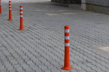 Renkli turuncu koniler, taşlarla döşenmiş kaldırım boyunca düzgün bir şekilde durarak, açık kentsel alandaki yayalar için temiz bir yol oluşturarak, düşünceli şehir planlamasını vurguluyor..