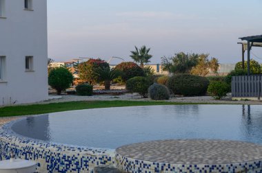 Durgun bir havuz kenarında, canlı bitkilerle ve alacakaranlıkta sakin bir atmosferle çevrili huzurlu bir anı yakalıyorum..