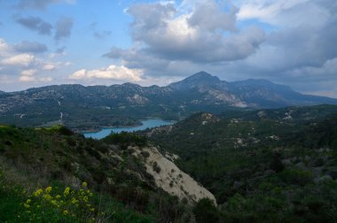 Yuvarlanan tepelerin nefes kesici manzarası ve dramatik bulutların çerçevelediği sakin bir göl. Bereketli yeşillik ve canlı kır çiçekleri bu huzurlu kırsal bölgeyi öğleden sonra aydınlığında zenginleştirir..